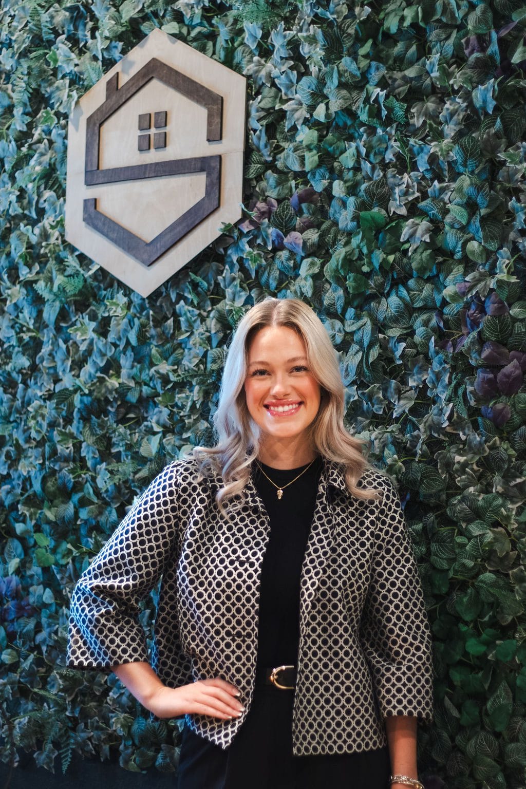Hayley Shaver, Practice Manager, smiling in front of the Social House greenery wall
